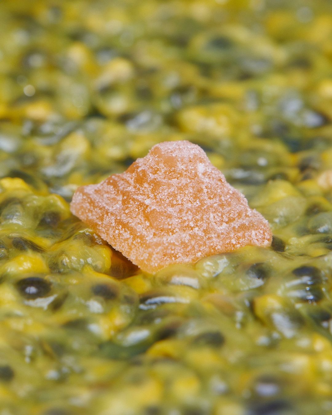Close-up shot of a candied ginger piece resting on passion fruit pulp with seeds, highlighting the textures and colors of the ingredients.