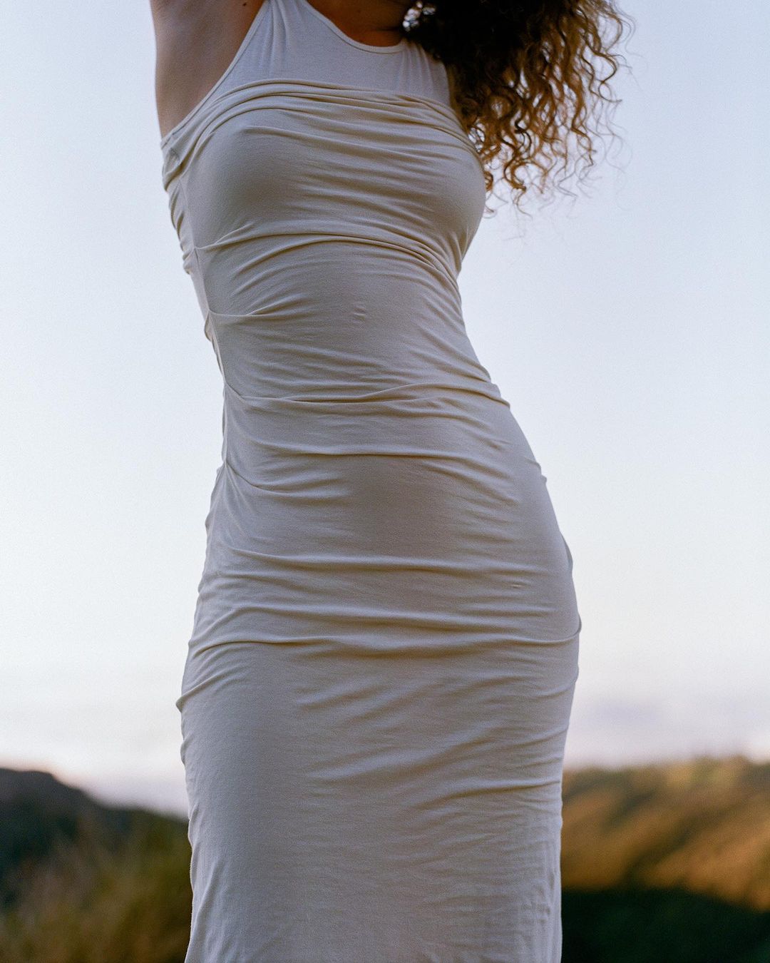 Close-up portrait of a woman wearing a cream halter neck dress outdoors against a distant natural horizon background