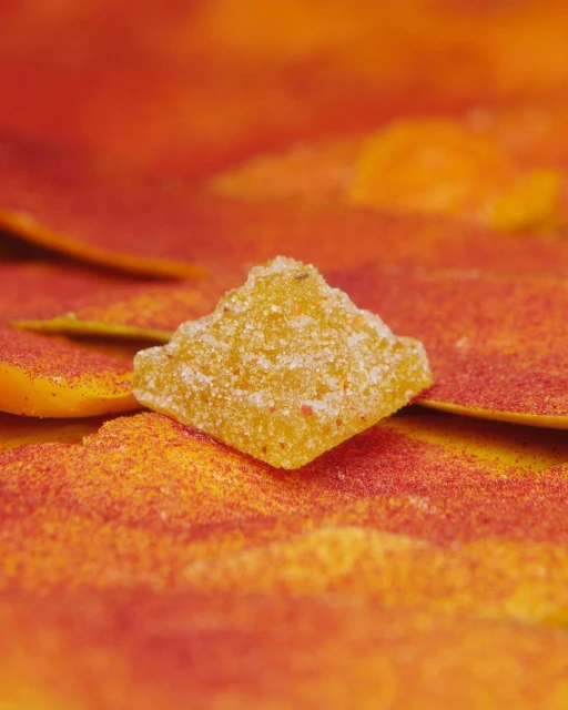 Macro shot of crystallized ginger candy on a textured orange surface, highlighting its sugary coating and vibrant color.