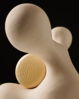 Close-up still life shot of a round Suavina lip balm tin resting on a white sculptural form, set against a dark background.