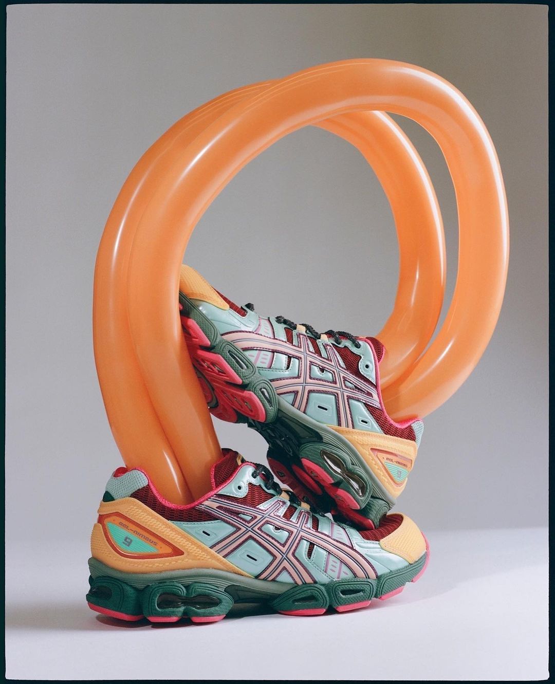 Two athletic shoes displayed with an orange balloon sculpture, showcased in a studio setting with diffused lighting and neutral backdrop.