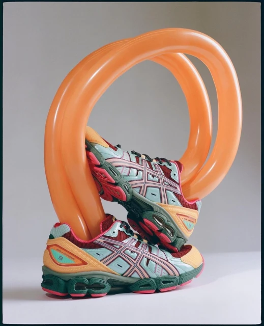 Two athletic shoes displayed with an orange balloon sculpture, showcased in a studio setting with diffused lighting and neutral backdrop.