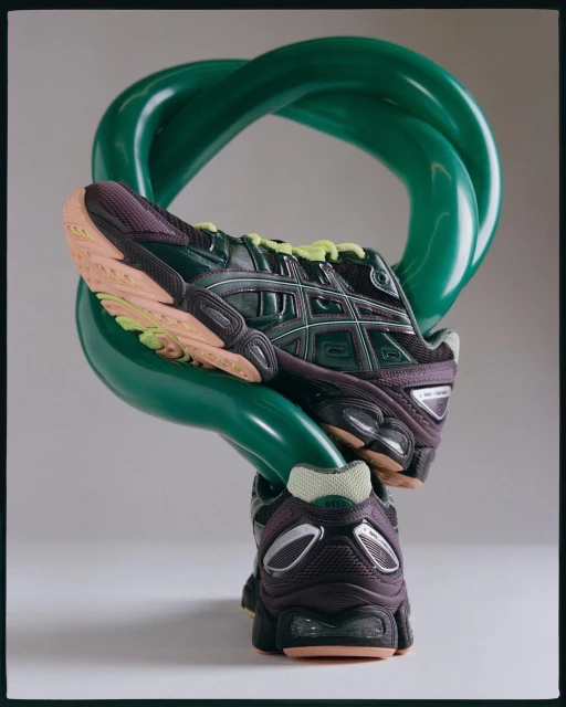 Close-up studio shot of an Asics running shoe balanced on a twisted green object, showcasing its design and athletic appeal.