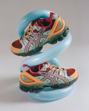 Two Asics running shoes are posed on a light blue inflatable object against a white background in a studio setting. Product photography.