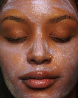 Close-up portrait of a woman with a skincare mask on her face. The soft lighting and shallow depth of field focus on her features.