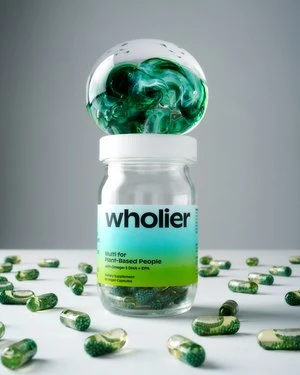 Still life shot of a clear supplement bottle with green label and green and white capsules on a white surface, studio lighting.