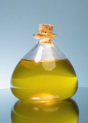Close-up studio shot of golden liquid in a clear glass bottle with a cork stopper reflecting on a shiny surface.