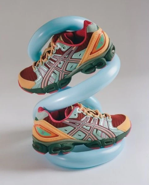 Two running shoes displayed with a blue, twisted, tubular shape in the center against a light grey background in a product shot.