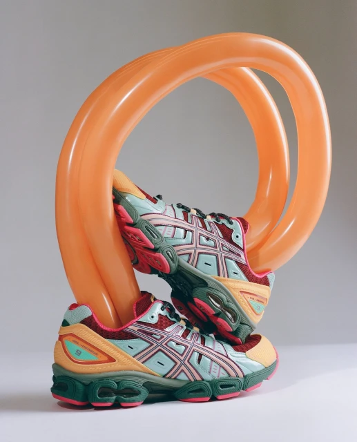 Two athletic shoes are stacked, intertwined with an orange balloon, showcasing a blend of sport and playful design on a plain background.