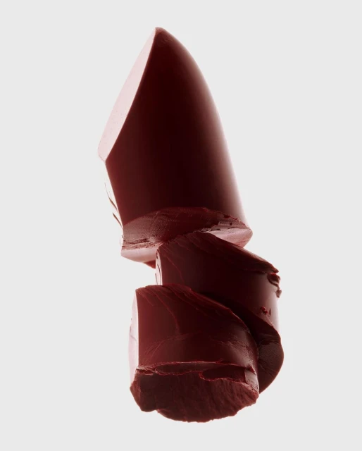 Macro shot of a sliced dark red lipstick on a white background, product photography for beauty and cosmetics advertising.