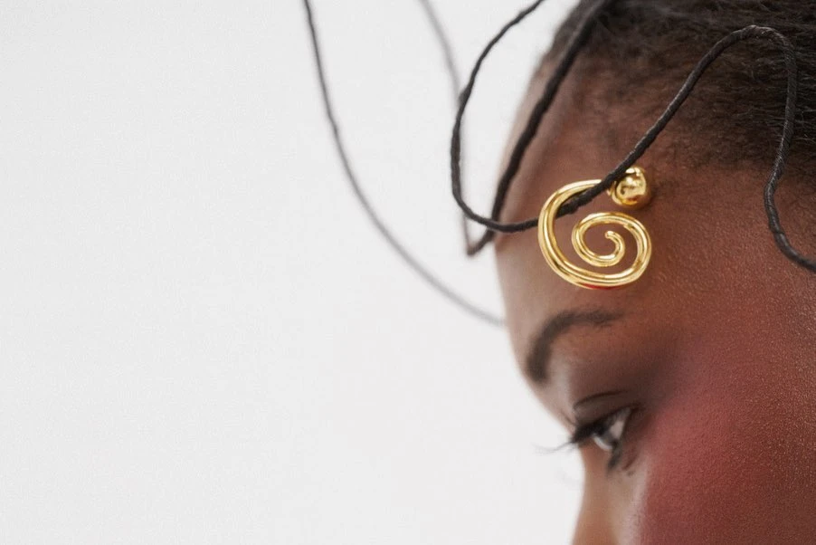 Close-up of an adult female's face with dark hair, wearing a unique gold earring, set against a pristine white backdrop.