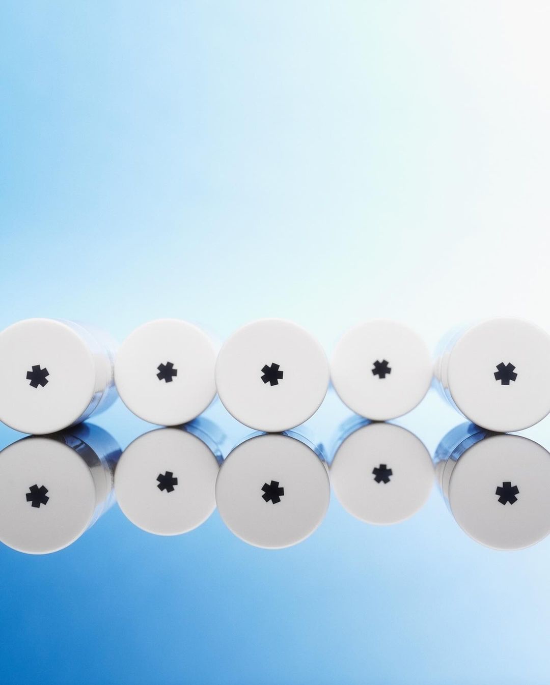 Five white cylindrical containers with black asterisk symbols lined up on a reflective surface against a gradient blue background.
