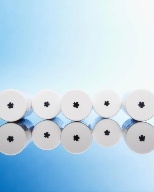 Five white cylindrical containers with black asterisk symbols lined up on a reflective surface against a gradient blue background.