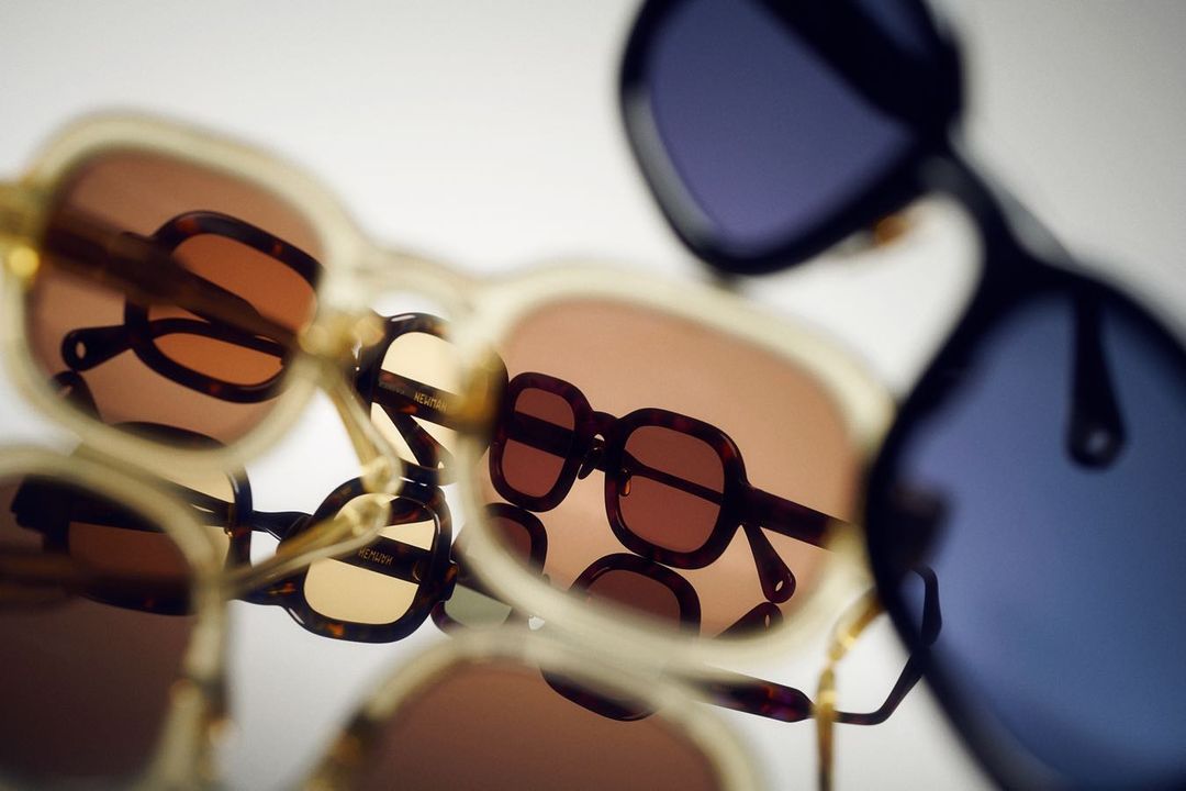 Multiple pairs of stylish sunglasses with brown and blue lenses are arranged and stacked on a white background, creating an abstract pattern.