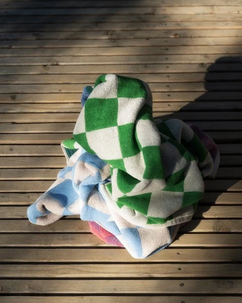Folded pile of patterned towels in green, white, pink, and blue sitting on a wooden deck in the sunlight with shadows.