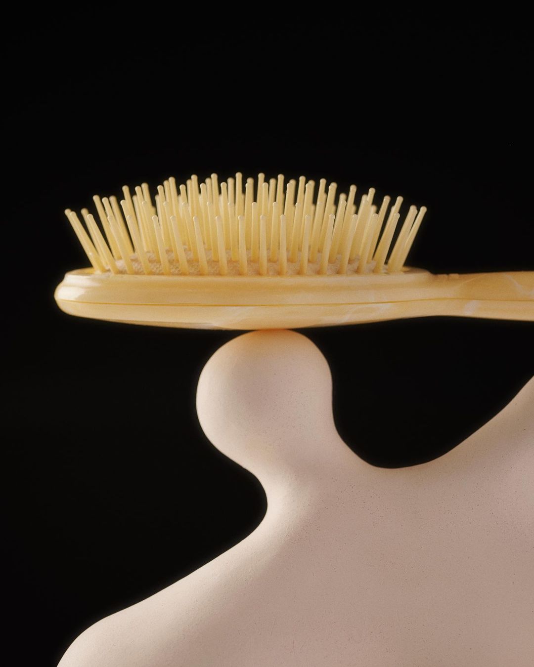 Close-up studio shot of a hairbrush balancing on a plaster bust against a stark black background, showcasing simplicity and balance.