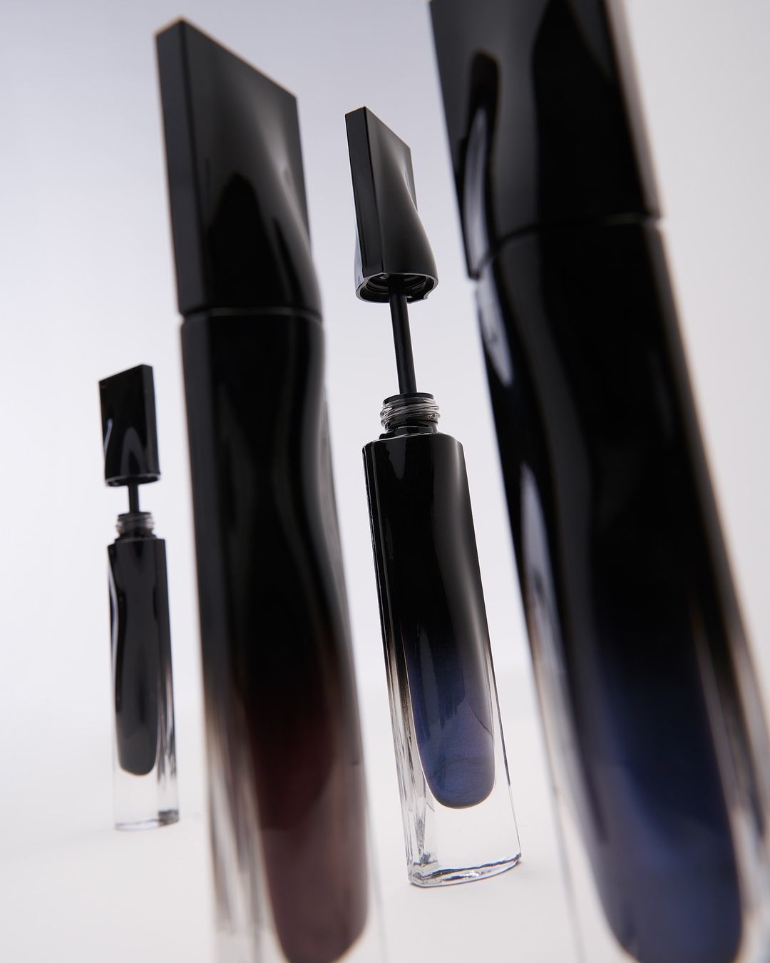 Multiple black mascara tubes with clear bases are arranged in a studio setup, showcasing beauty and cosmetic products.
