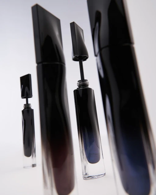 Multiple black mascara tubes with clear bases are arranged in a studio setup, showcasing beauty and cosmetic products.