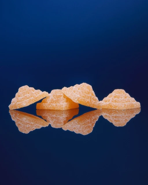 Close-up of a set of orange, pyramid-shaped gummies on a reflective surface against a dark blue background with a shallow depth of field.
