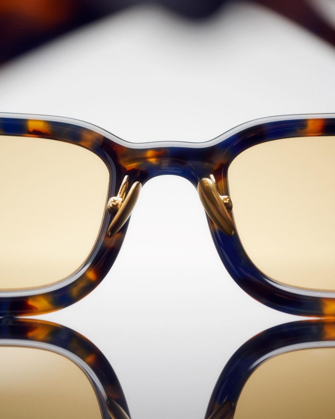 Close-up studio shot of tortoise shell-patterned eyeglasses with gold nose pads and yellow lenses against a white backdrop, showcasing eyewear details.