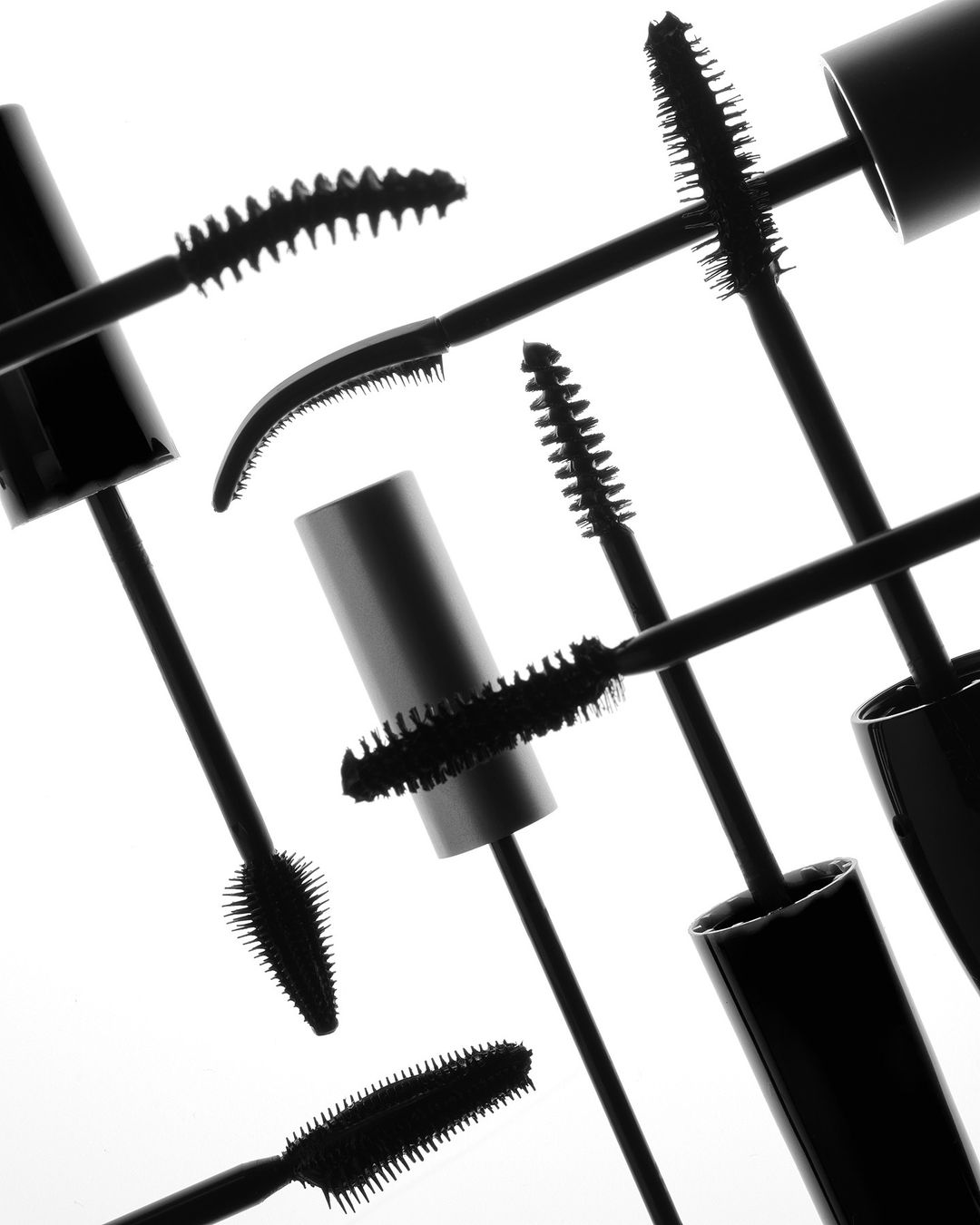 Close-up studio shot featuring an arranged collection of mascara brushes and tubes against a bright, neutral background for beauty advertising.