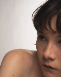 Close-up portrait of a young person with dark hair and freckles against a neutral white background