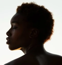 Profile silhouette portrait of a black woman with short curly hair against a bright white background.