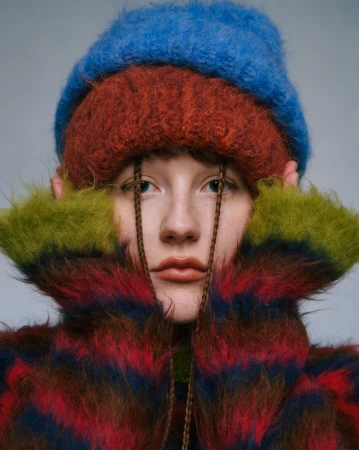 Close-up portrait of a woman wearing layered fuzzy colorful knit hats and a matching textured sweater.