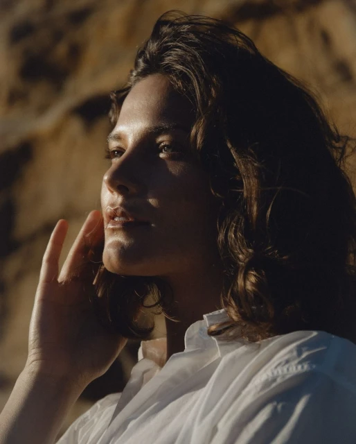 Portrait of a brunette woman in a white shirt against a blurred brown background, showcasing natural light and soft-focus aesthetic.