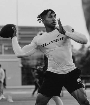 Football player in action: Quarter view of a young man throwing a football, wearing athletic wear, on a light outdoor field.