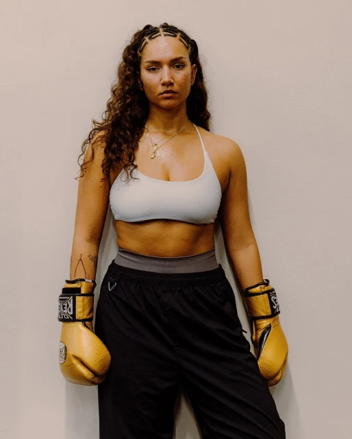 Attractive female athlete with curly hair and boxing gloves in athletic wear posing in front of a white wall. Athletic, sporty, fitness concept.