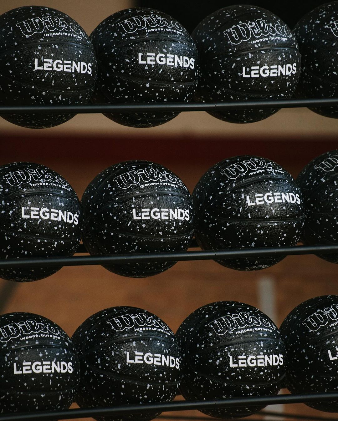 Close-up of black Wilson volleyballs on a rack with 'Legends' printed on them, indoor setting, showcasing sports equipment.