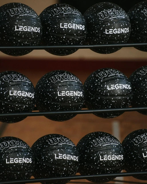 Close-up of black Wilson volleyballs on a rack with 'Legends' printed on them, indoor setting, showcasing sports equipment.