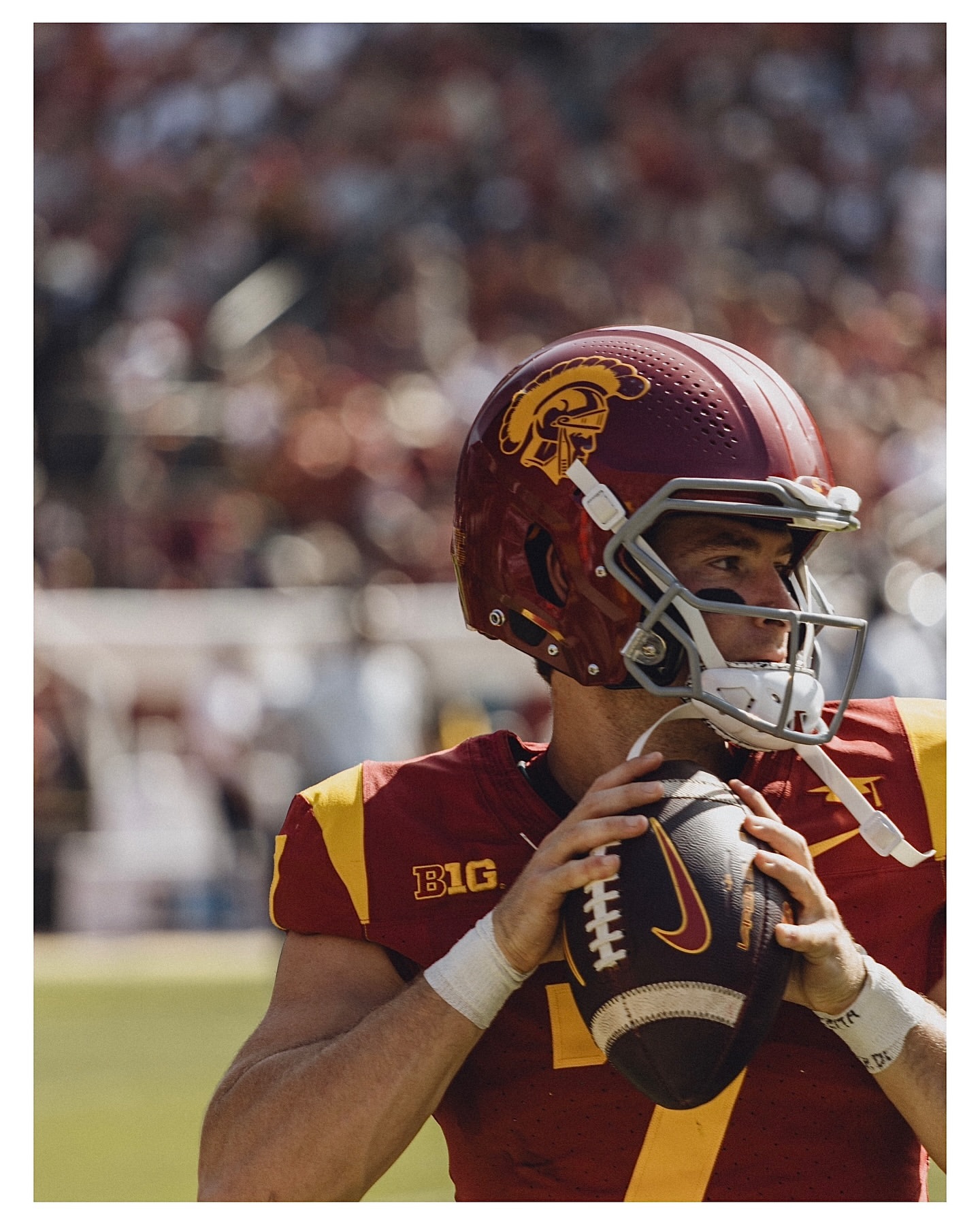 Football quarterback in a burgundy and gold uniform prepares to throw the ball on a sunny day, captured in a waist-up shot.