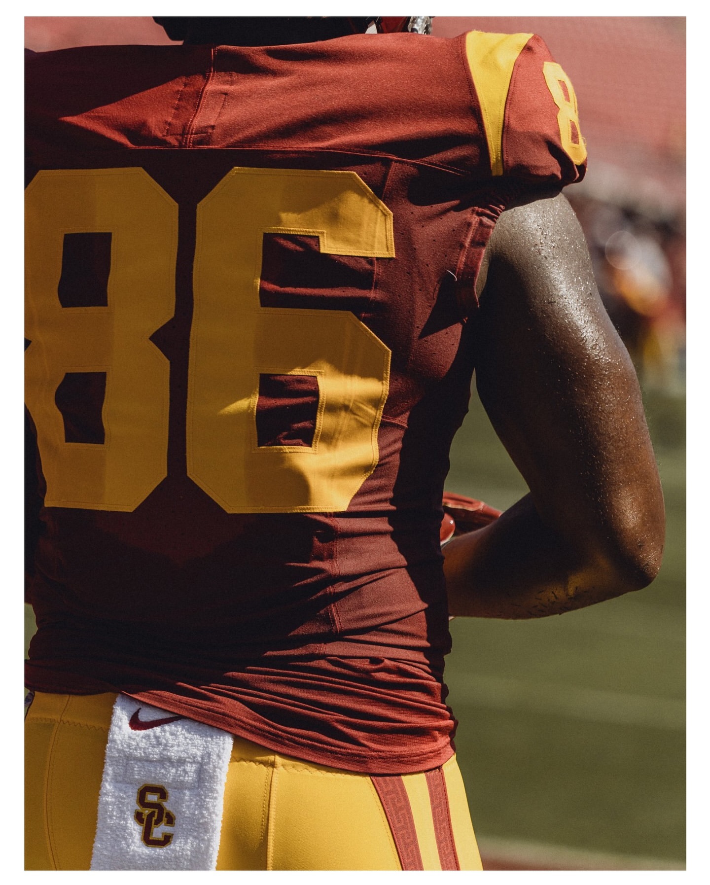 American football player in uniform with number 86 stands on field during daytime under bright lighting, wearing maroon and gold uniform.