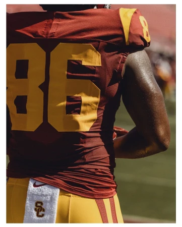 American football player in uniform with number 86 stands on field during daytime under bright lighting, wearing maroon and gold uniform.