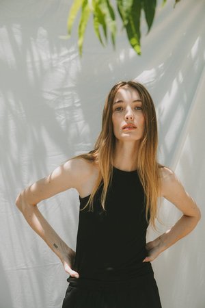 Woman in black top posing against a white draped backdrop with tropical leaf shadows above