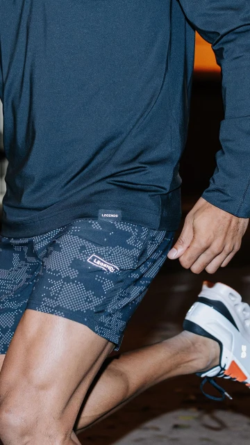 Close-up shot of a person wearing a long sleeve shirt and running shorts, and running shoes on pavement, with a blurred background.