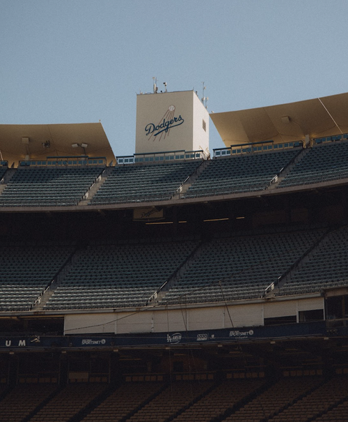 View of Dodger Stadium featuring empty green seats and the Dodgers logo set against a clear blue sky, capturing a quiet moment.