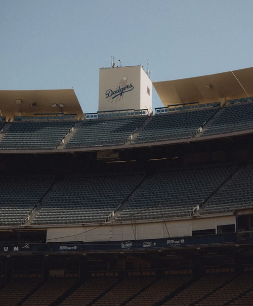View of Dodger Stadium featuring empty green seats and the Dodgers logo set against a clear blue sky, capturing a quiet moment.