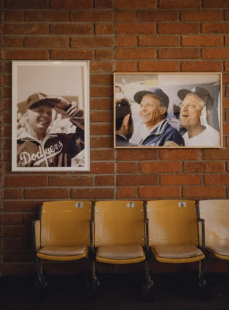 Interior brick wall with framed photos of Dodgers players and yellow stadium chairs. A nostalgic nod to baseball history.