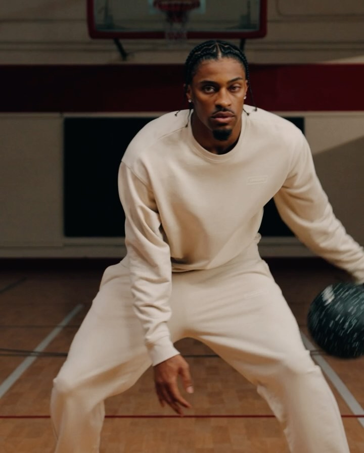 Man wearing cream sweatshirt and matching sweatpants dribbling a basketball on an indoor court.