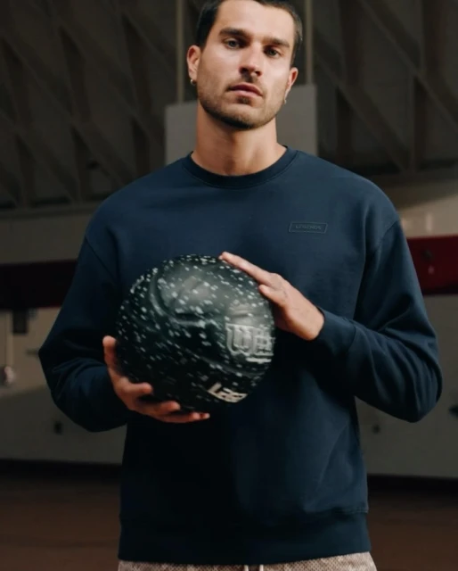 Athletic man in a blue sweatshirt holding a Wilson basketball indoors, posing in a gymnasium with natural light.