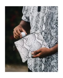 Man in snakeskin print polo shirt holding a golf ball and a matching pouch by Kris Ryan