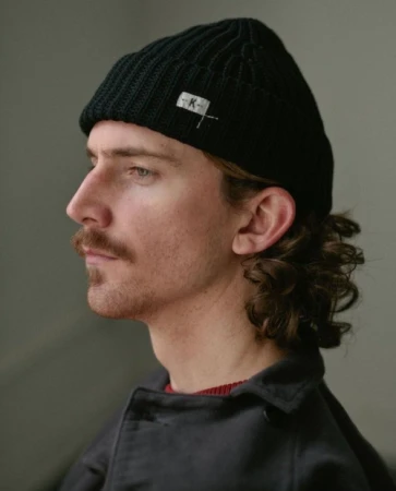 Profile portrait of a man with a mustache wearing a black ribbed beanie and dark jacket photographed by Kris Ryan