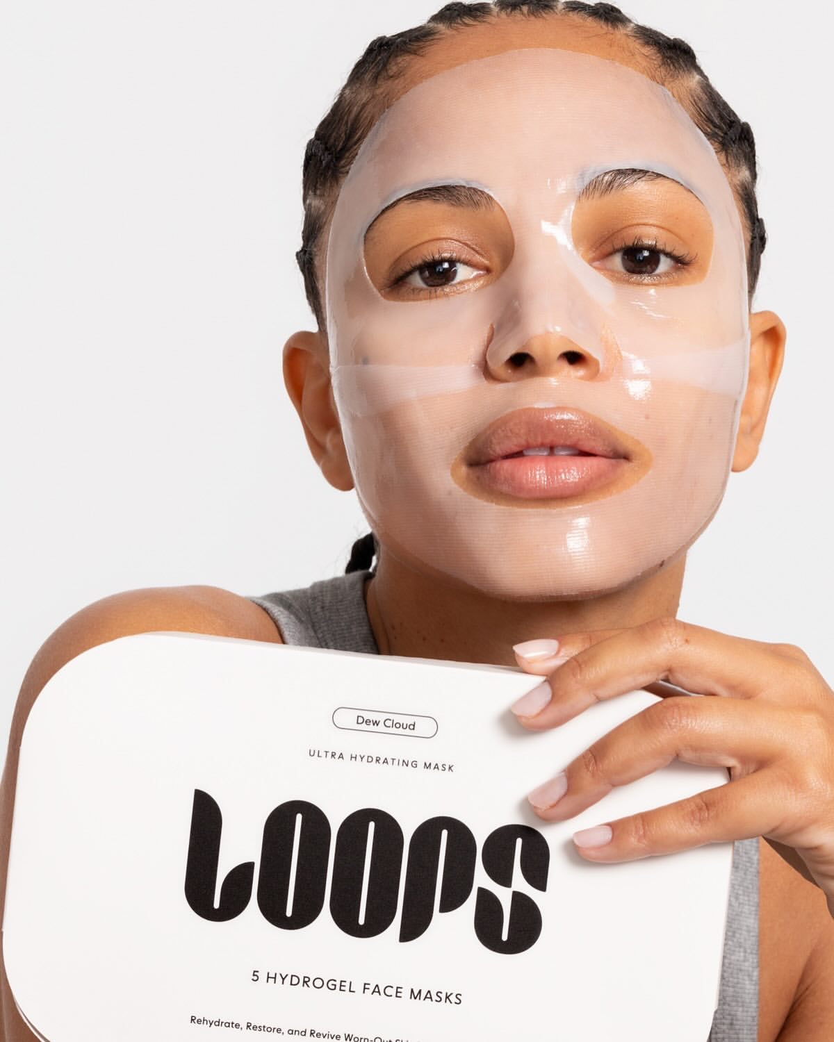 Close-up of a woman with a sheet face mask holding a Loops face mask package, promoting beauty and skincare treatments.
