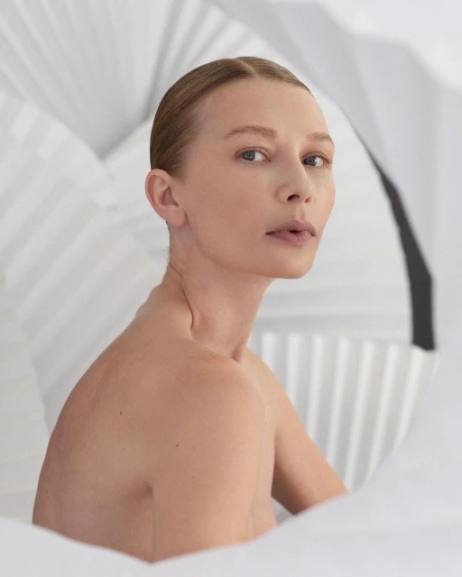 Close-up studio shot of a young adult female, looking at the camera with a neutral expression, and set against a background of white folded paper.