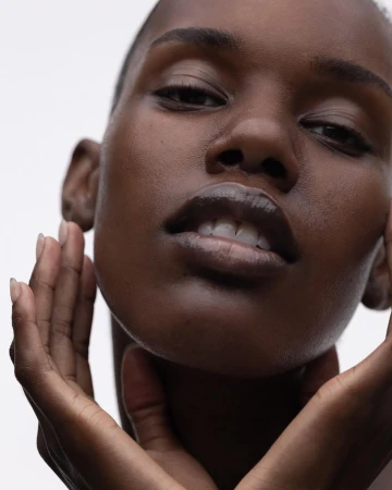 Close-up beauty portrait of a Black woman holding her hands to her face against a plain white background