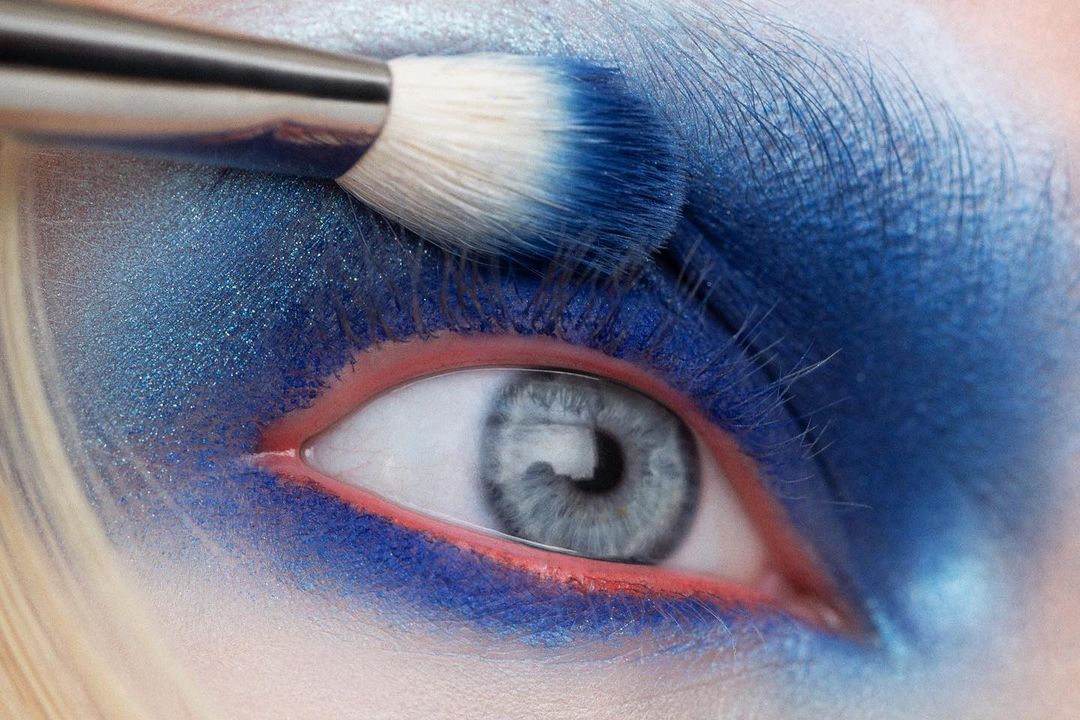 Close-up of woman's eye with blue eyeshadow and makeup brush applying pigment. Beauty shot, fashion, eye makeup, cosmetic product.