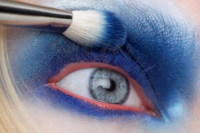 Close-up of a blue eye makeup application with a brush by Angela Marklew